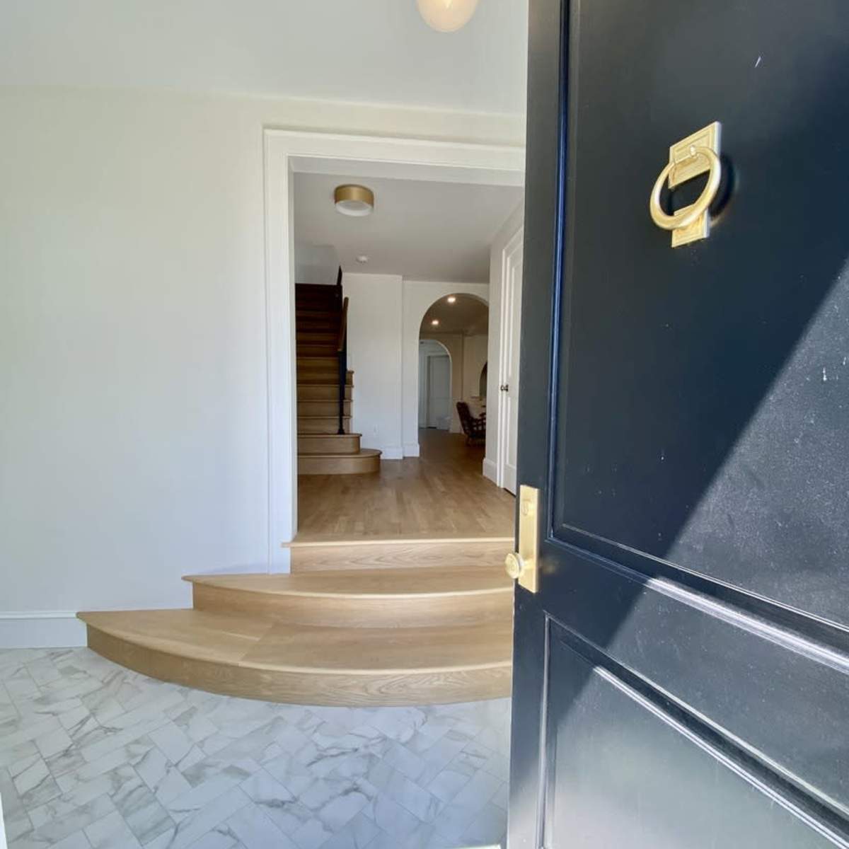 A black front door opens to reveal a spacious entryway with curved wooden stairs leading to the upper floor.