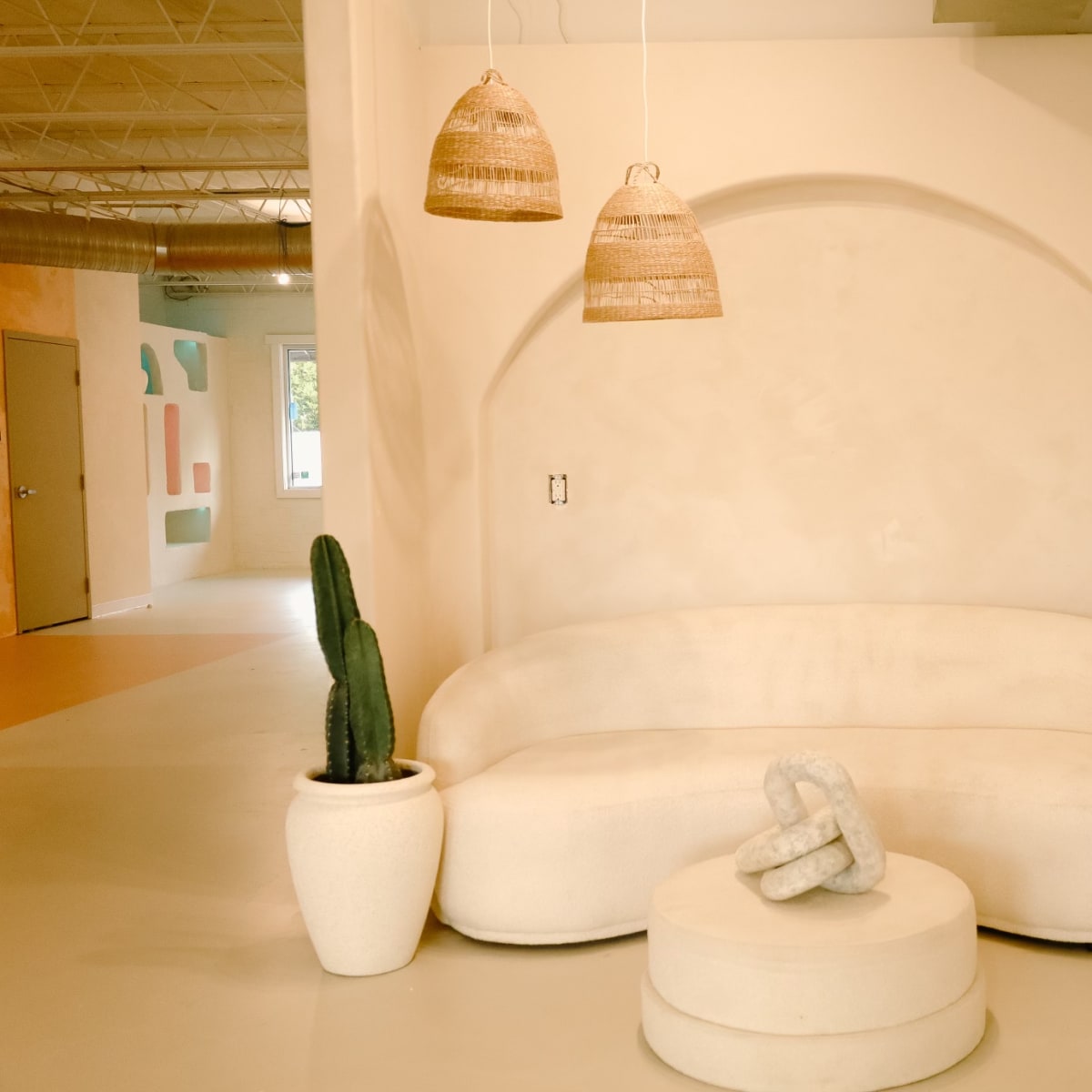 A soft, neutral-toned seating area features a curved sofa and round coffee table, flanked by two potted cacti.
