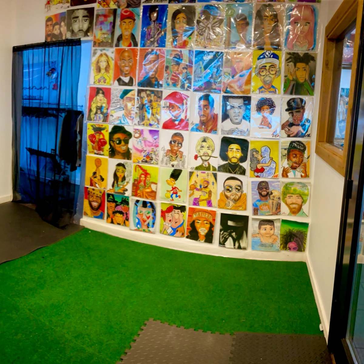 A room with a green carpet area, black mats on the floor, and a wall covered in colorful portraits, alongside a banner and a blue curtain.