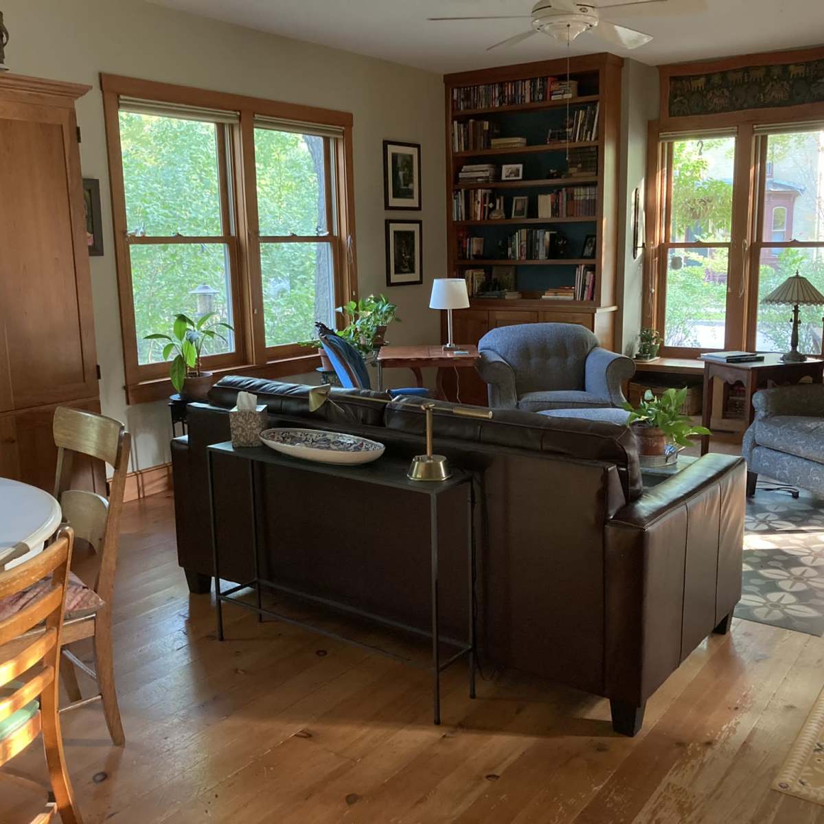 A cozy living room with wooden floors, a variety of seating options, and large windows letting in natural light.