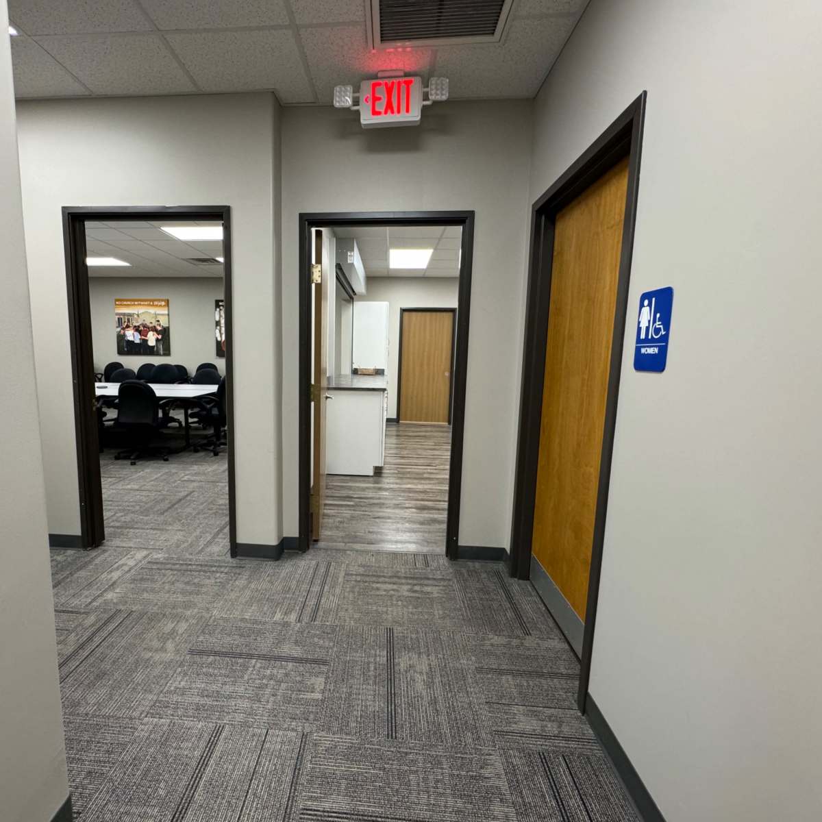 A hallway with doorways leading to a conference room and a restroom, with exit signs visible above.