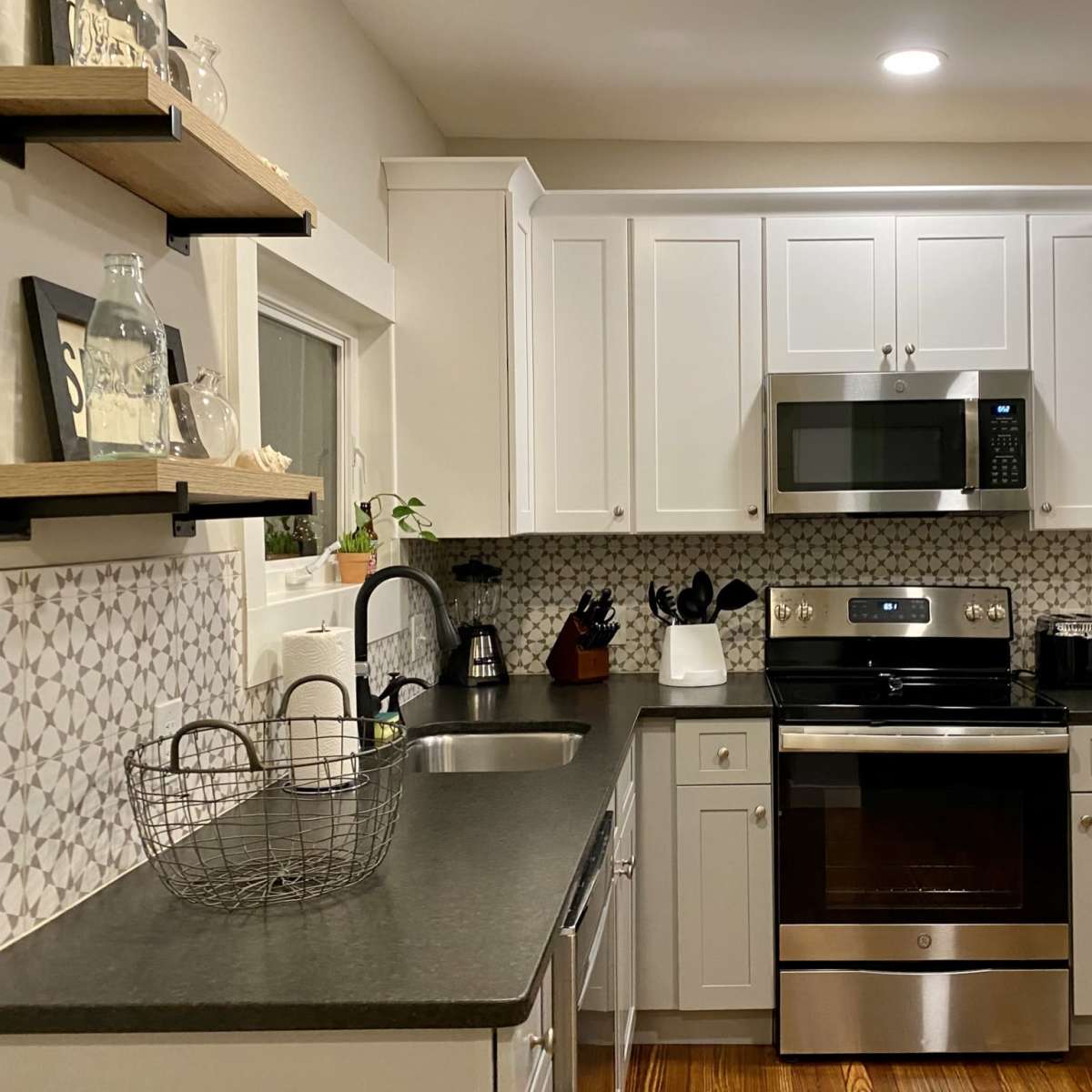 A modern kitchen featuring white cabinetry, a stainless steel microwave and oven, a black countertop, and patterned backsplash tiles.