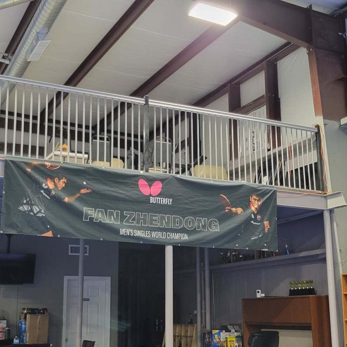 An indoor sports facility featuring a banner for Fan Zhendong, with a two-story structure and various shelves displaying items.