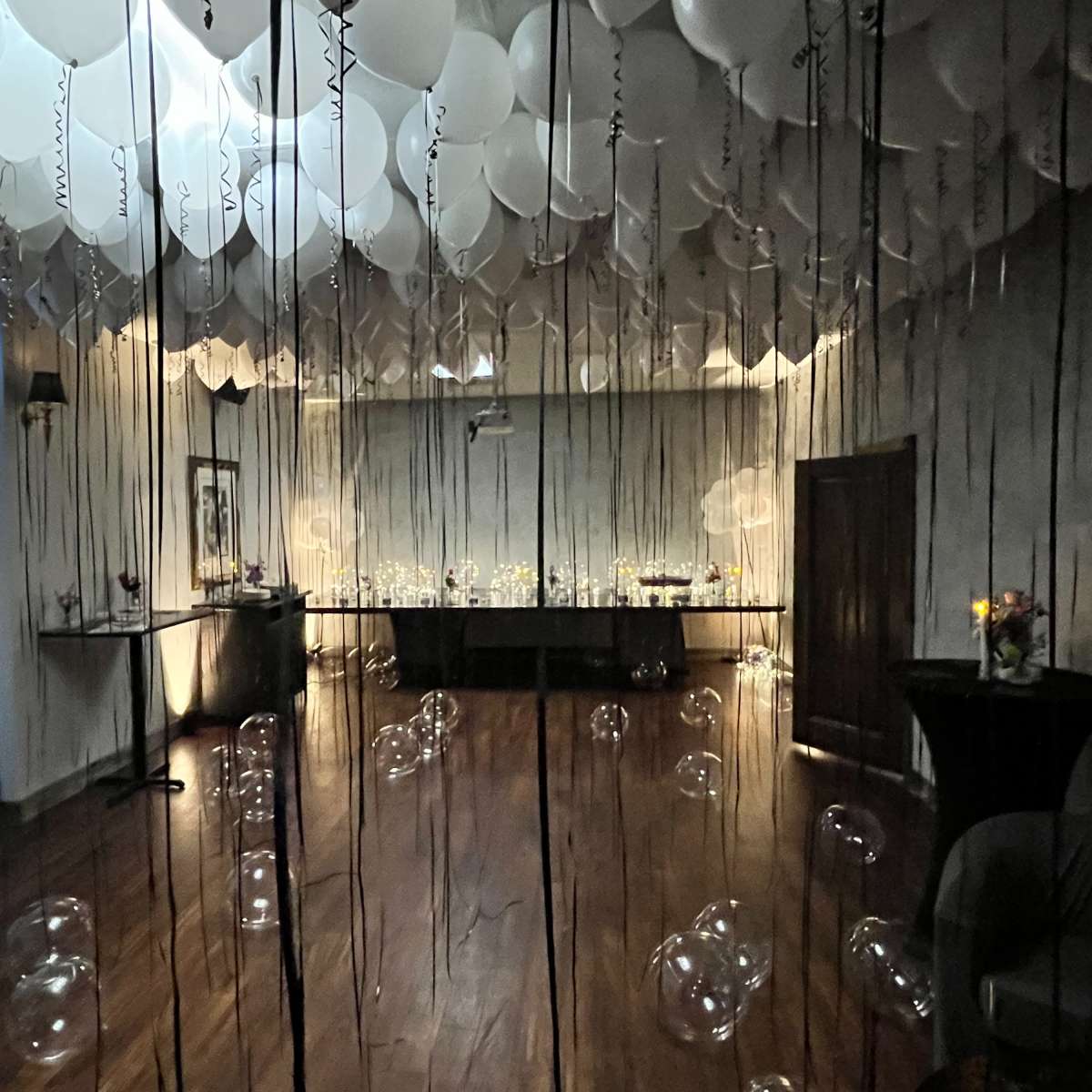 The scene features a dimly lit event space decorated with white balloons hanging from the ceiling and elegant tables set with candles.