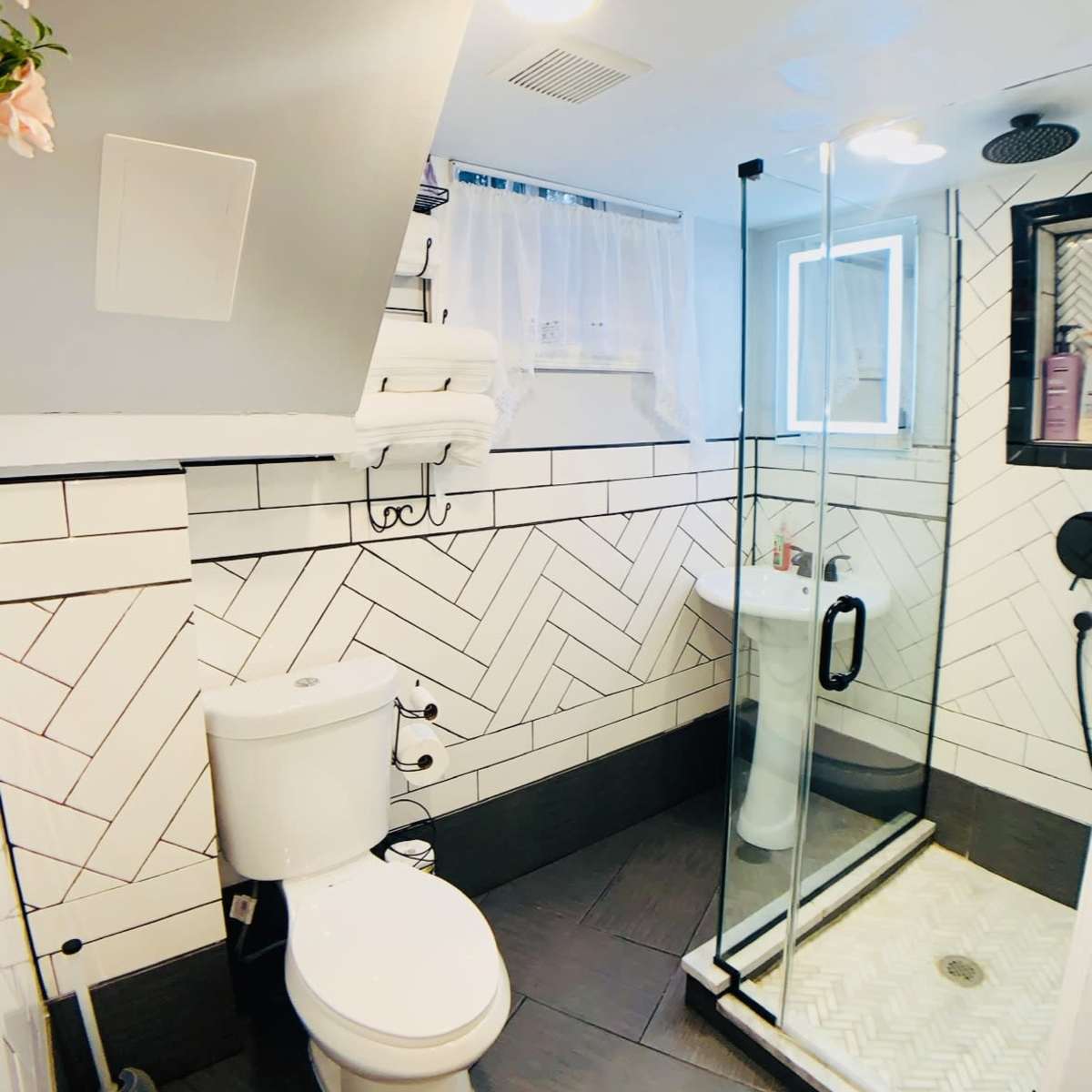 A modern bathroom featuring a glass shower stall, a toilet, and a herringbone-patterned tile wall.