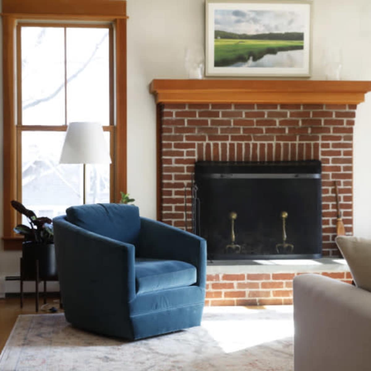 A cozy living room with a blue armchair facing a brick fireplace and shelves filled with books and decorative items.