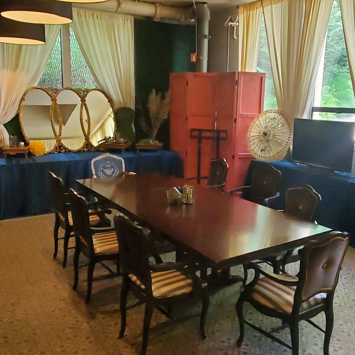 A meeting room with a long wooden table surrounded by chairs, decorated with plants and furnishings, and large windows letting in natural light.