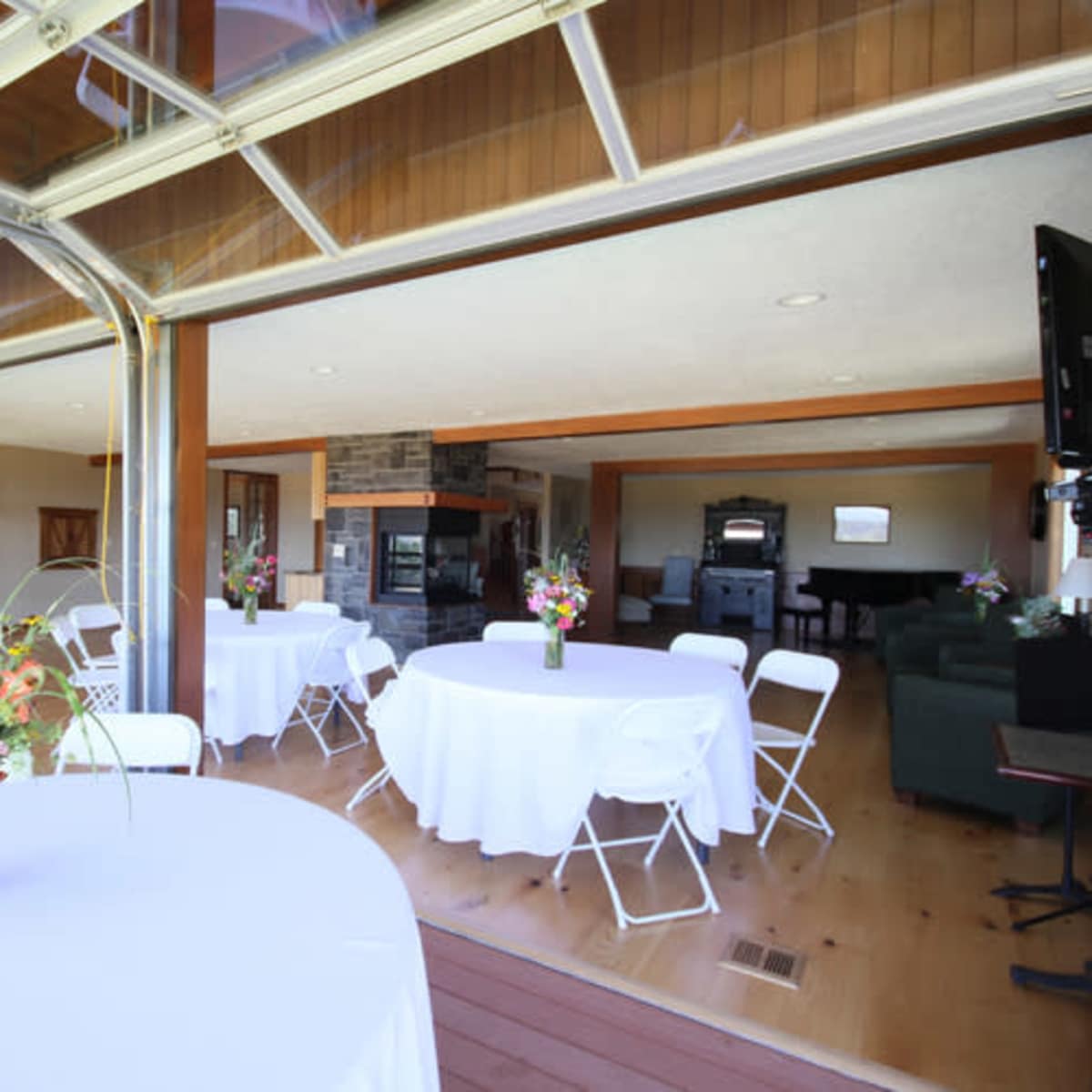 An indoor venue with tables set for an event, featuring large windows that open to an outdoor area.
