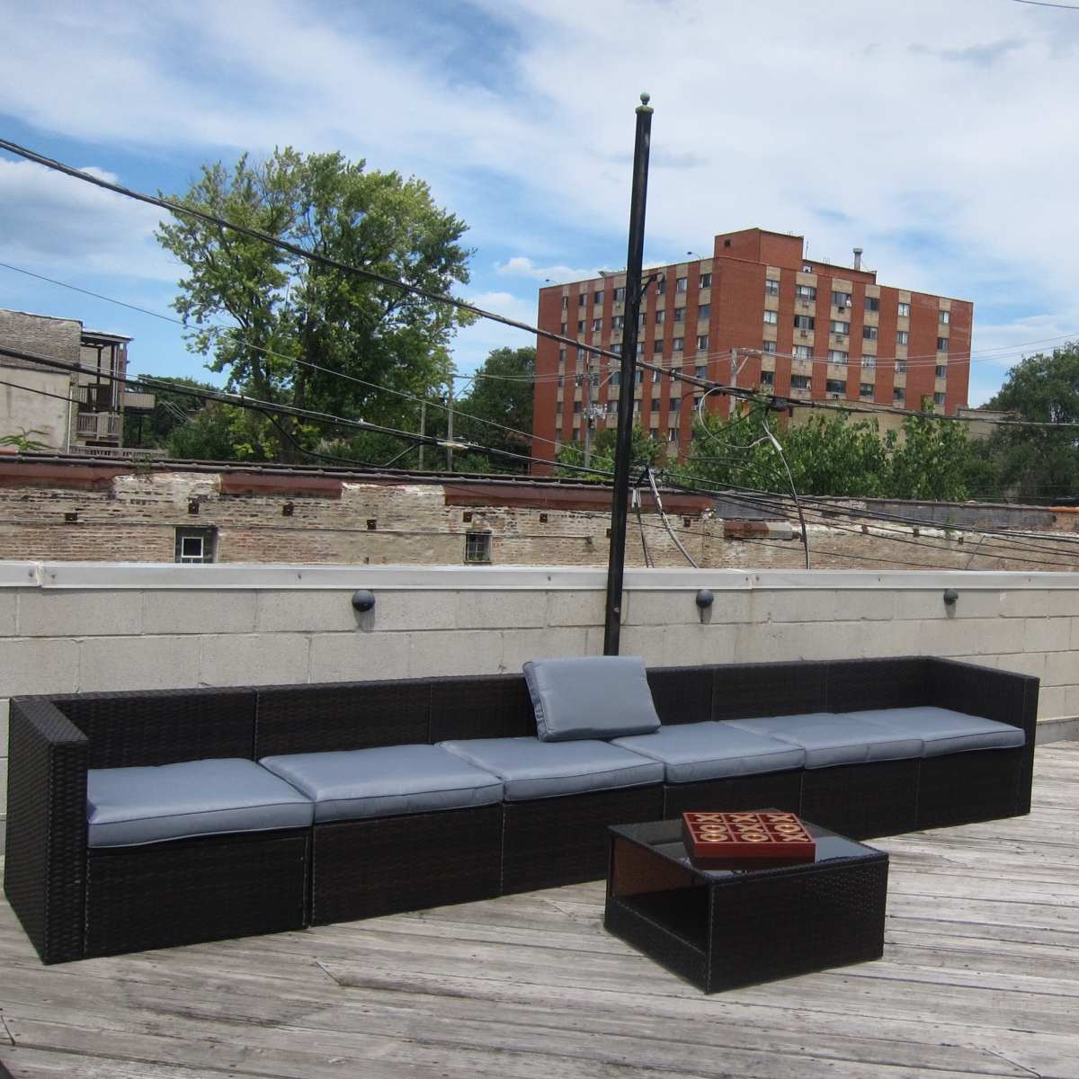 A rooftop area with a sectional couch and a small table made of wicker, surrounded by a concrete wall and power lines above.