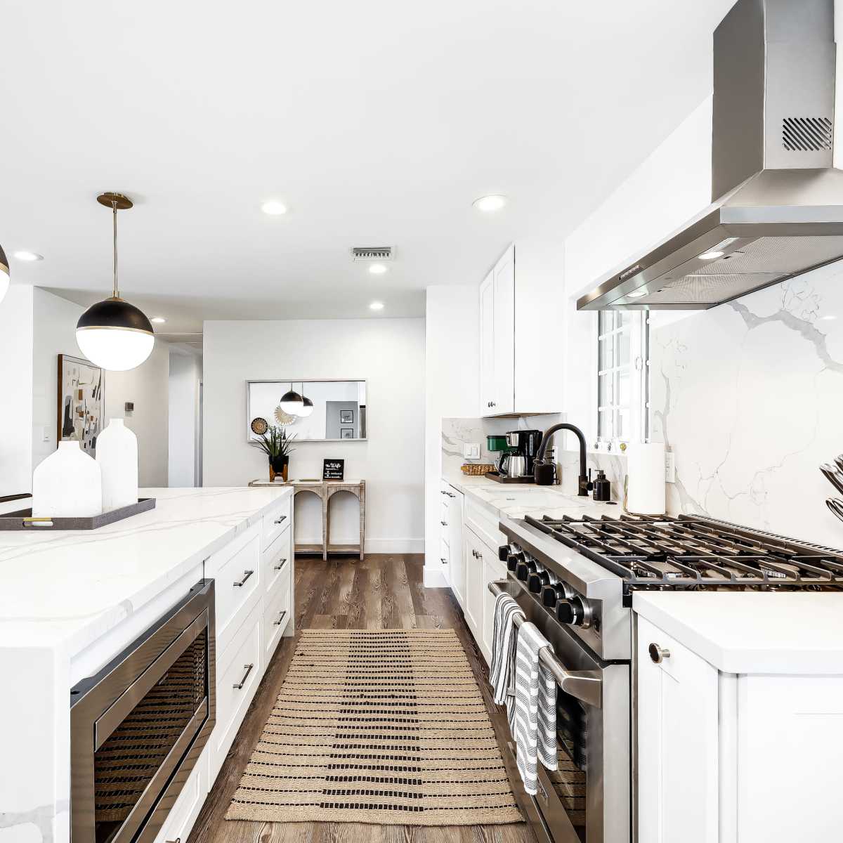 A modern kitchen features a central island with white marble countertops, stainless steel appliances, and pendant lighting.