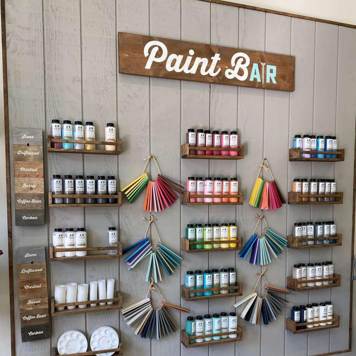 A wall display featuring organized paint bottles and color swatches at a paint bar.