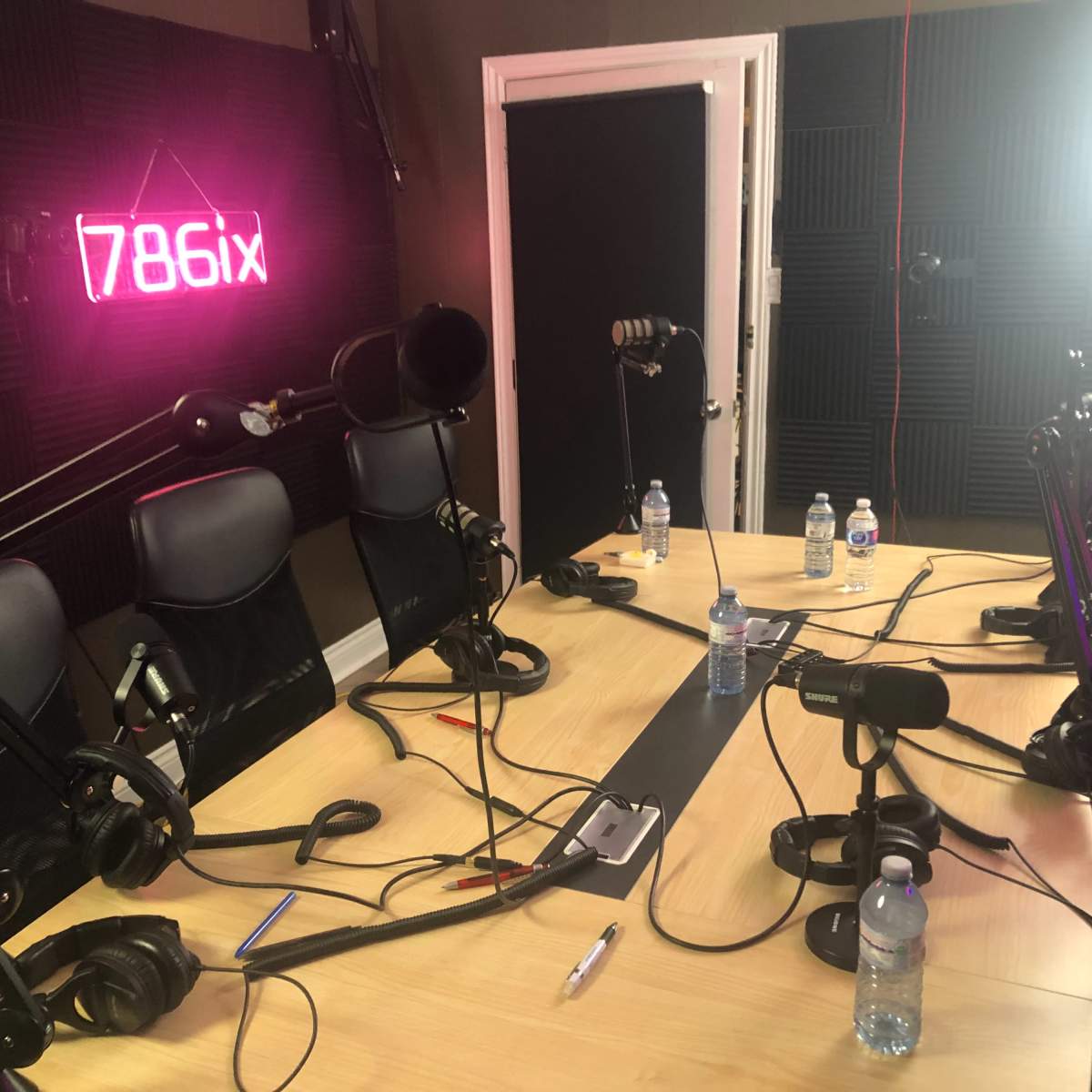 A podcast recording studio with microphones, headphones, and water bottles on a wooden table.