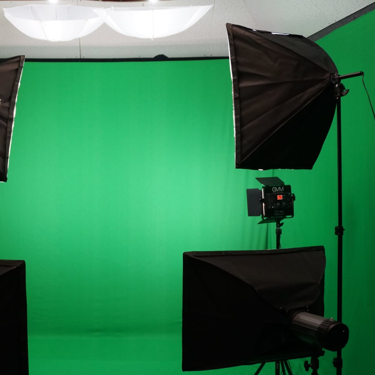 A photography setup with two softbox lights positioned on either side of a green backdrop, complemented by two black monitors in front.