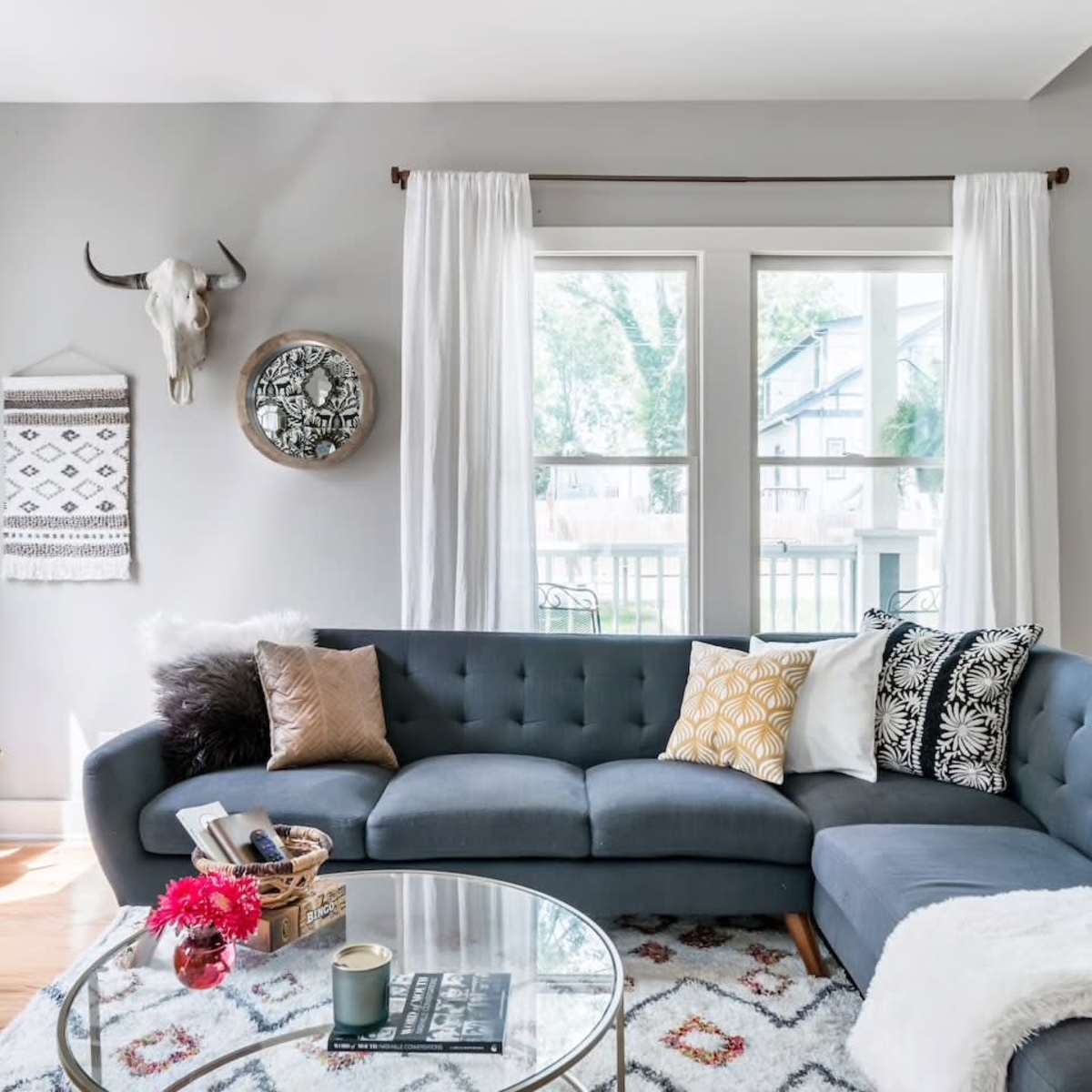 A cozy living room featuring a sectional sofa, a round coffee table, decorative pillows, and large windows that provide natural light.