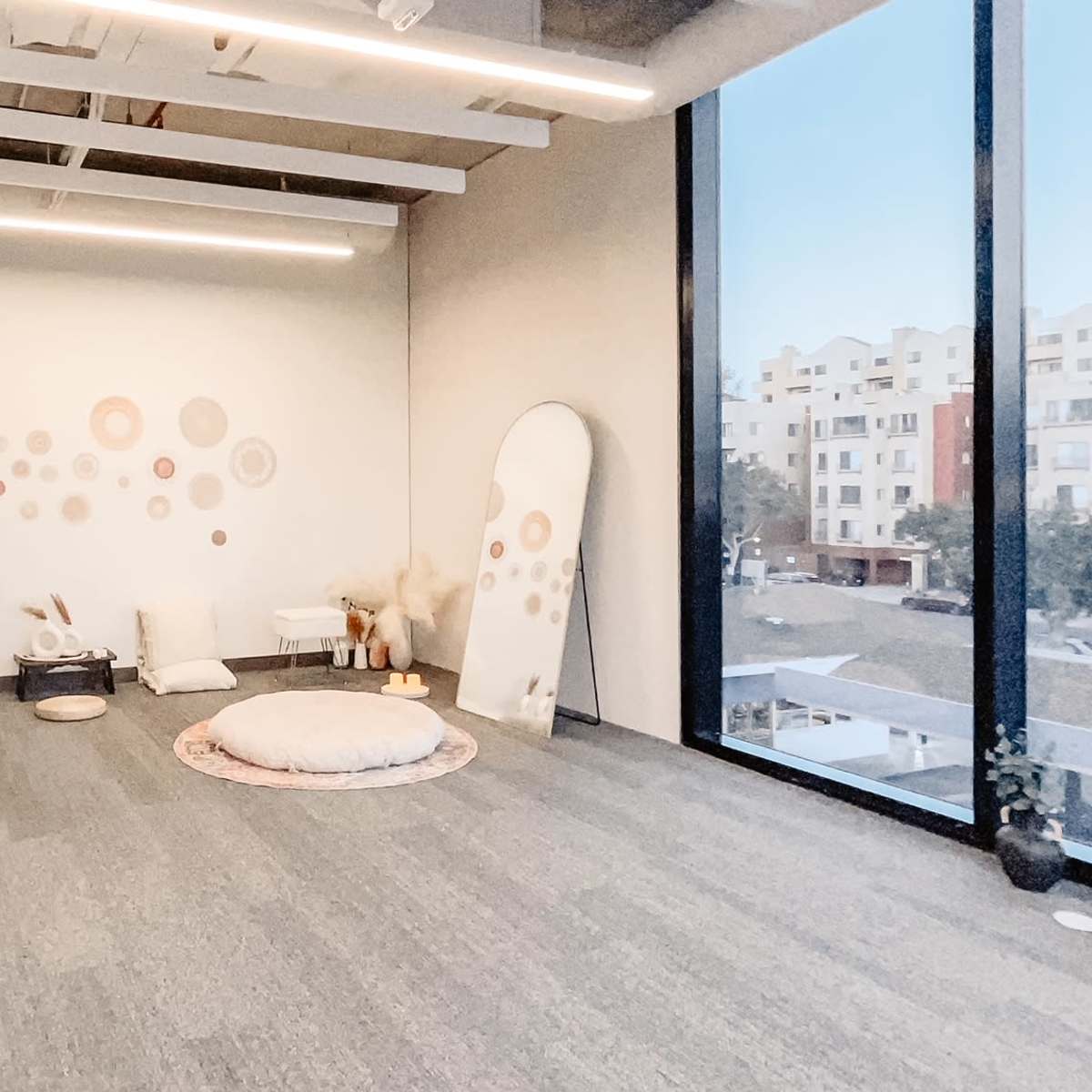 A minimalistic indoor space featuring a circular rug, cushions, and a large mirror against a wall adorned with decorative wall patterns.