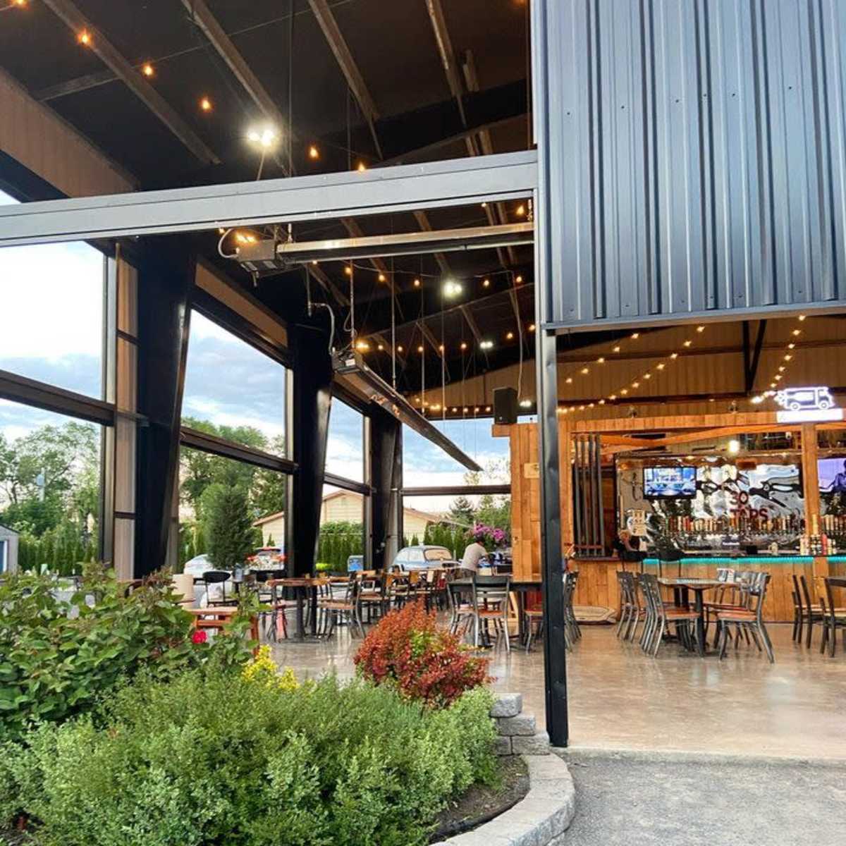 A modern restaurant with large open windows features outdoor seating, surrounded by landscaped plants and stone edging.
