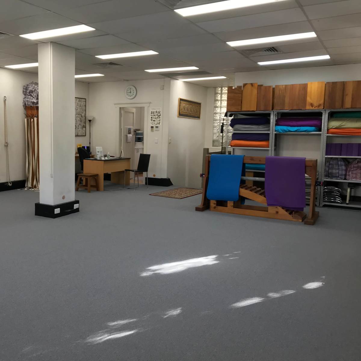 A spacious, well-lit studio with exercise ropes and colorful yoga mats neatly arranged on shelves.