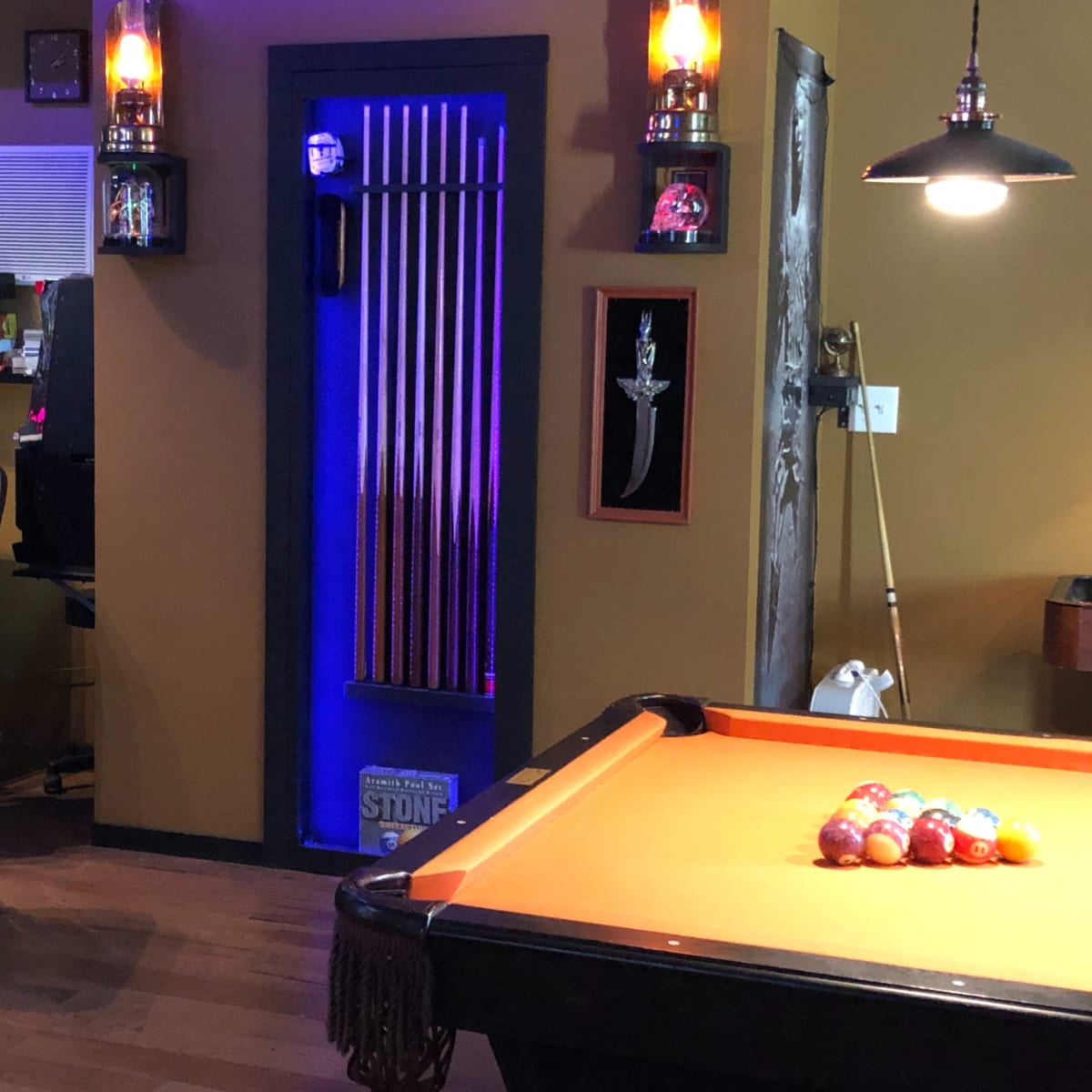 A game room with a pool table in the foreground, a poker table in the background, and a doorway lit with blue light.
