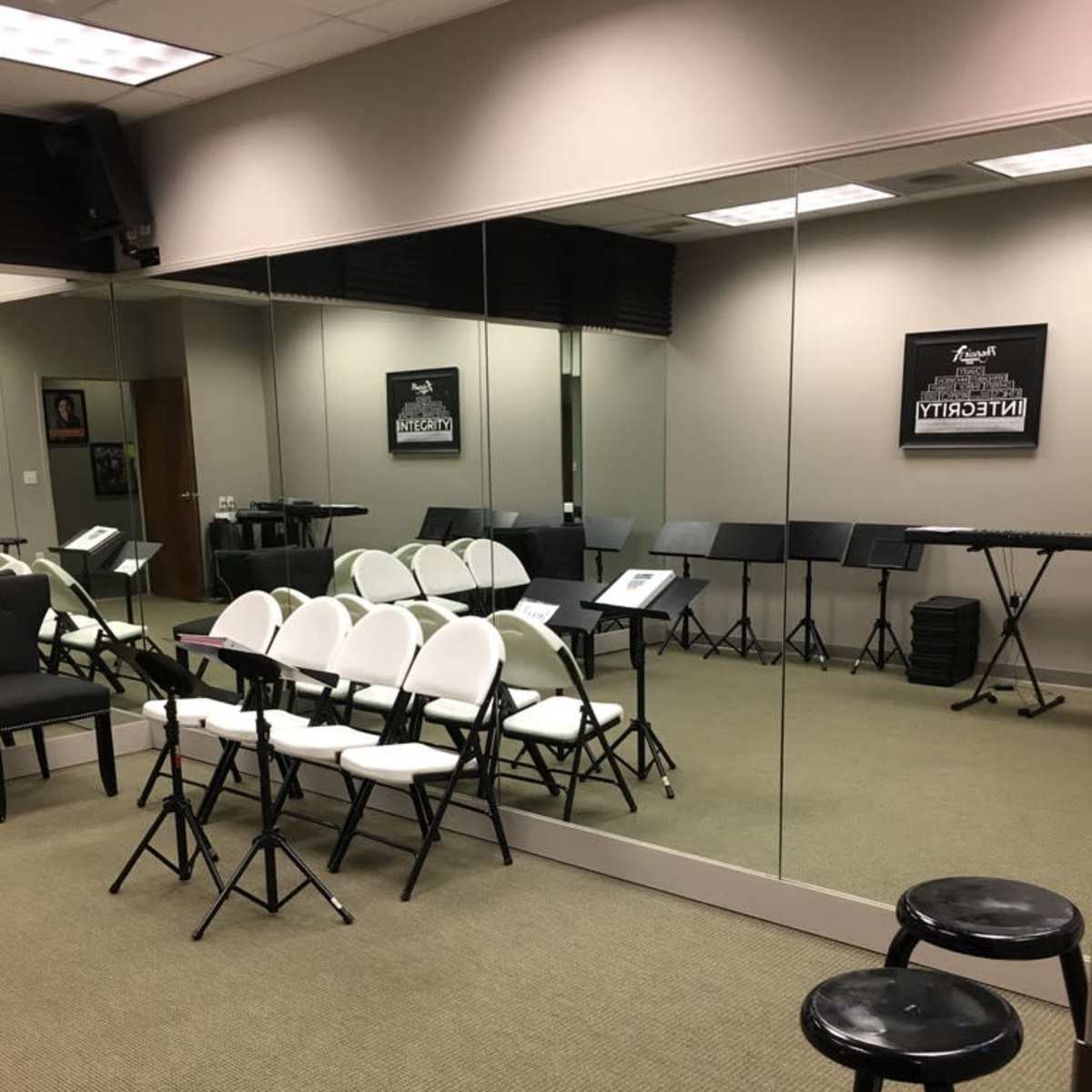 A music practice room features rows of white folding chairs, music stands, and a mirrored wall.