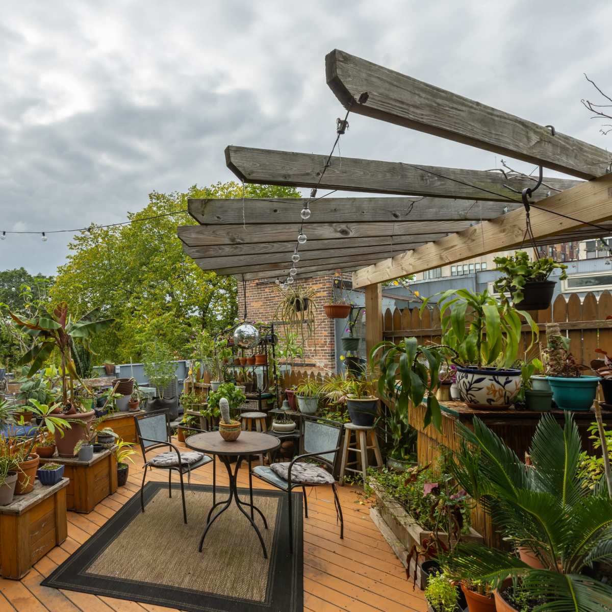 The rooftop terrace features a wooden pergola and is filled with various potted plants, seating arrangements, and decorative elements.