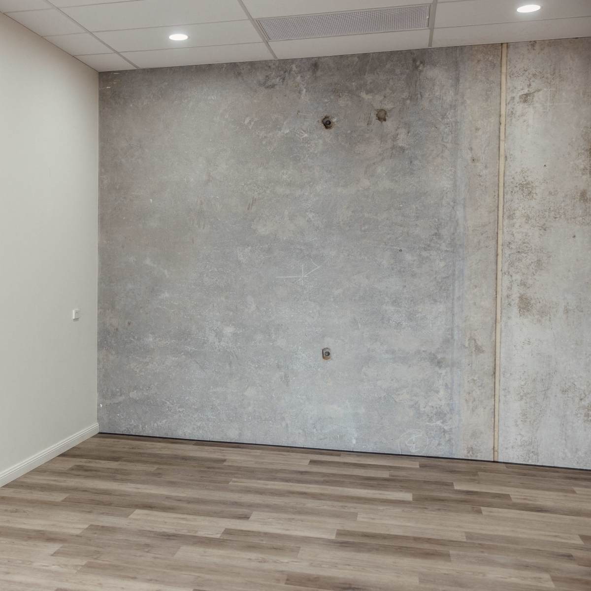 An empty room with one wall featuring a concrete finish and light-colored wooden flooring.