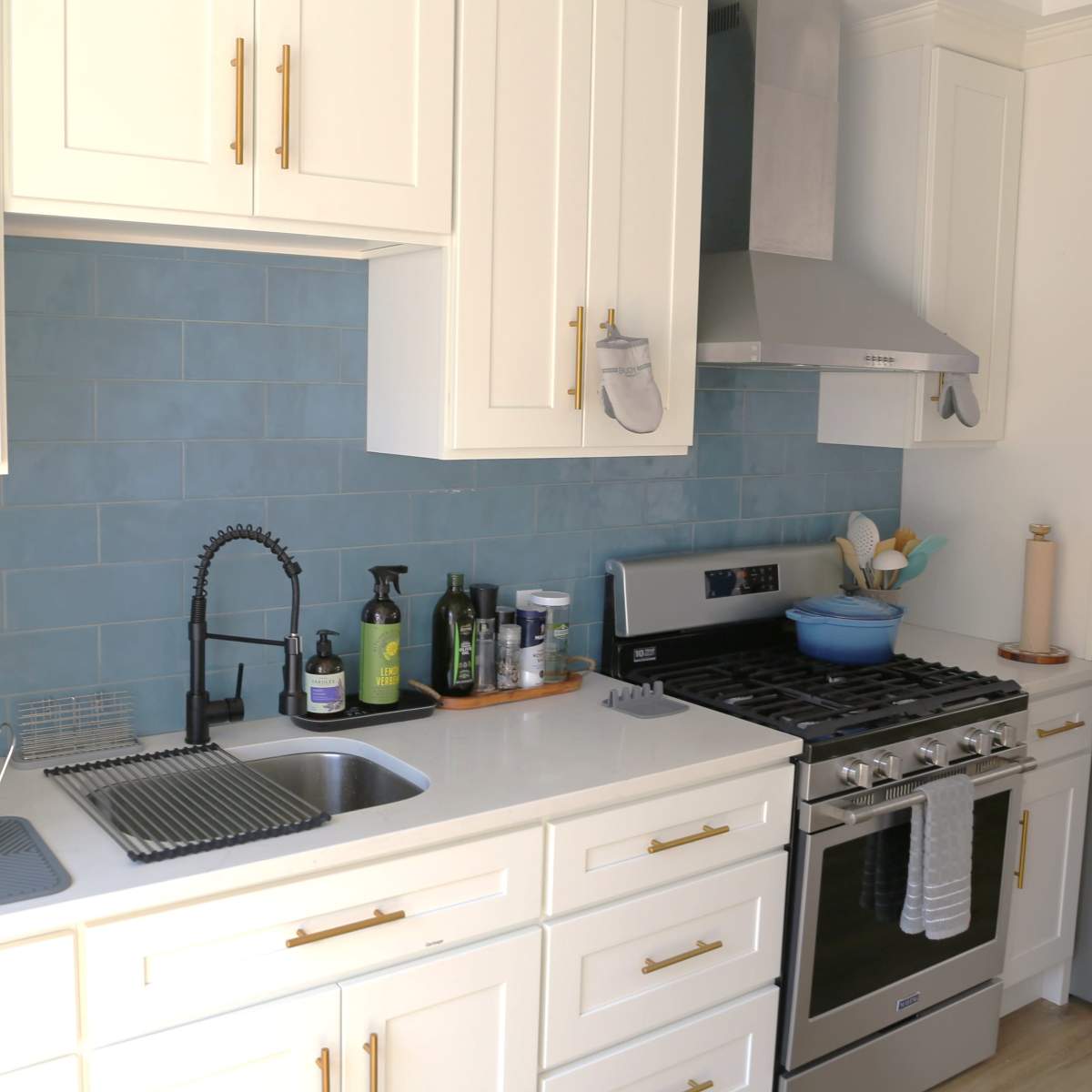 A modern kitchen features white cabinetry, a stainless steel refrigerator, a gas stove with a hood, and blue tile backsplash.