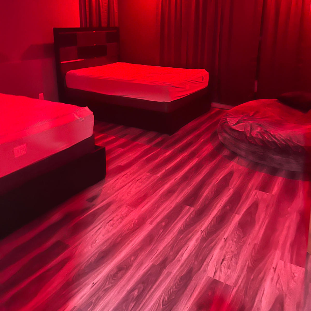 The room features two unmade beds, a bean bag chair, and dim red lighting.