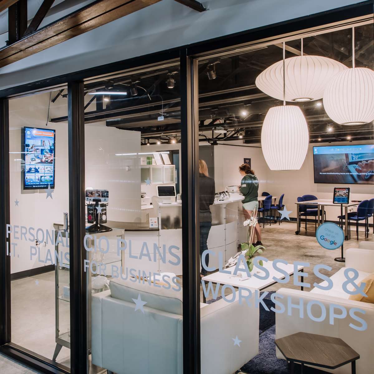 A modern office space with large windows, featuring seating areas and informational displays about classes and business plans.