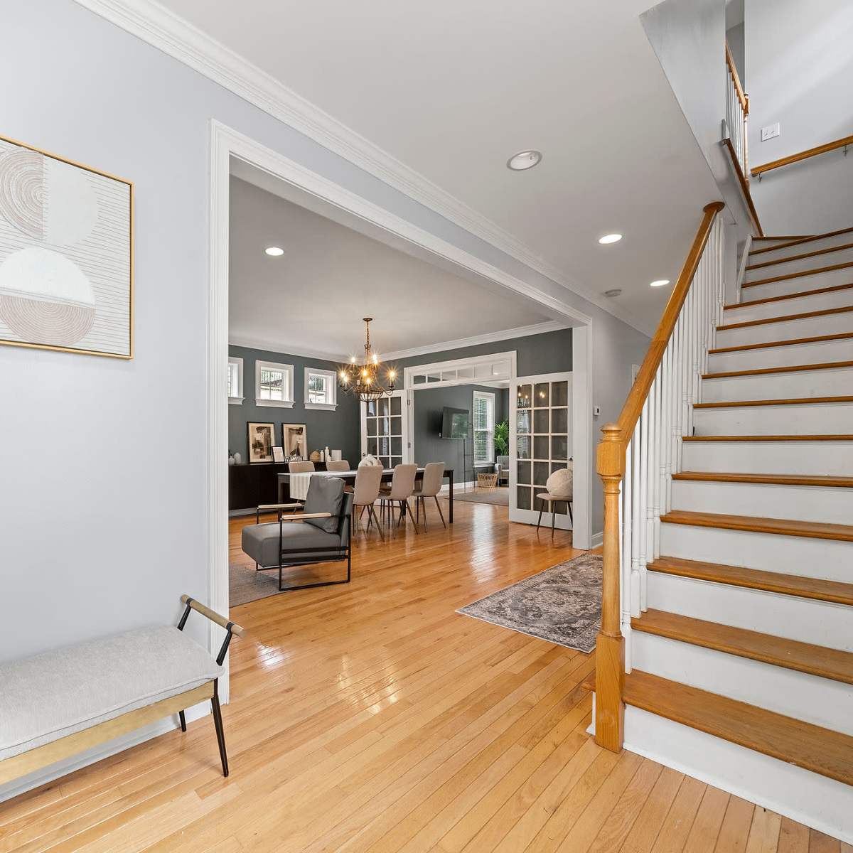 A well-lit entryway leading to a dining area, with a staircase on the right and modern artwork on the walls.