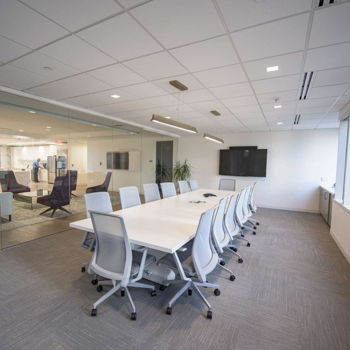 A modern conference room with a long white table surrounded by ergonomic chairs, featuring large windows and glass walls.