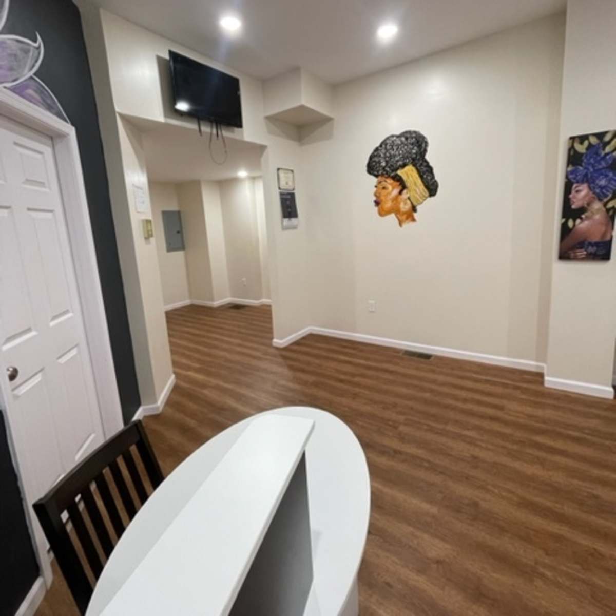 A small reception area with a desk, wooden flooring, and wall artwork depicting a profile of a woman.