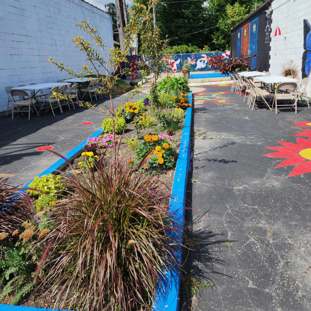 A colorful outdoor area with flower beds, seating arranged along the sides, and murals on the walls.