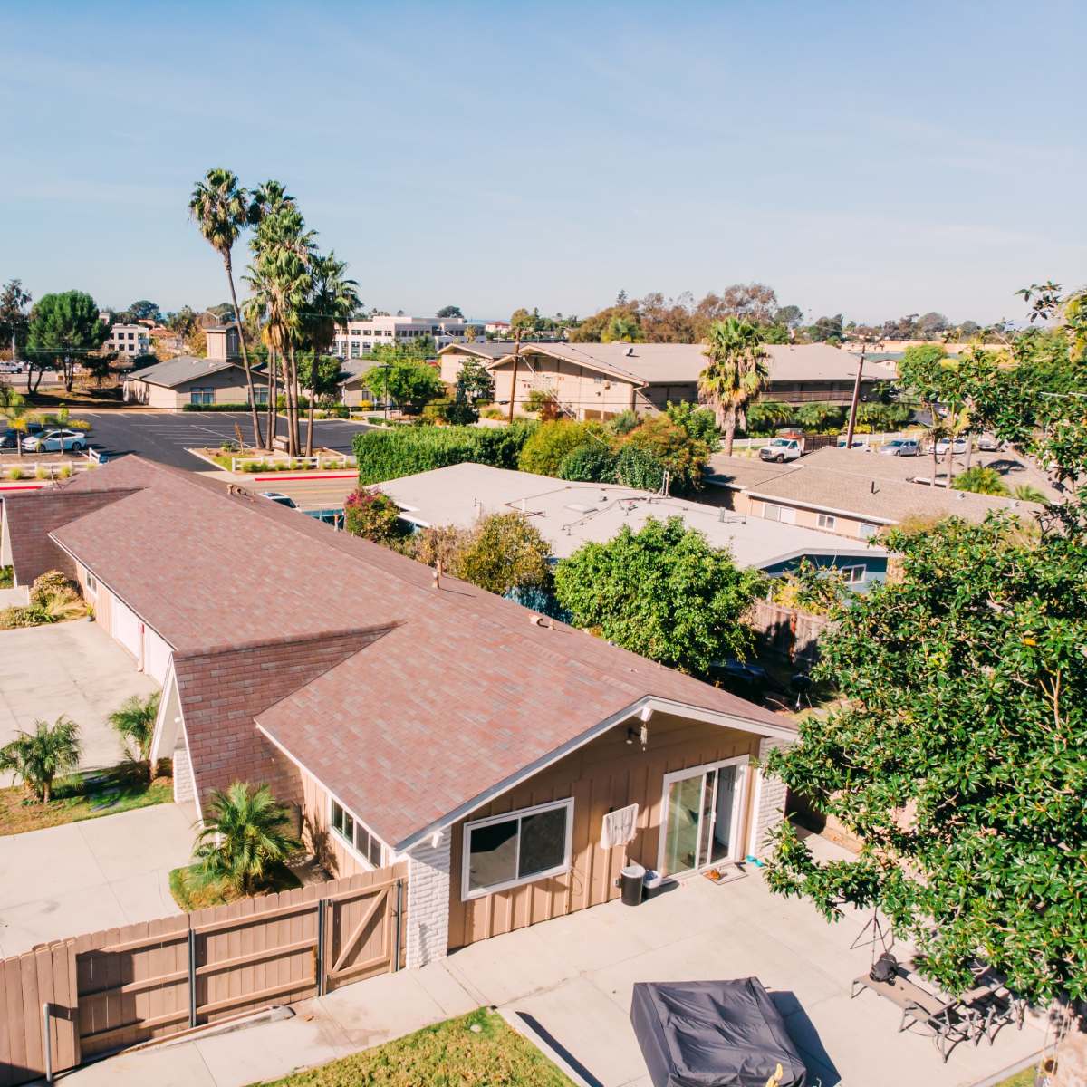 A residential area with single-story houses, palm trees, and parking spaces, viewed from an elevated angle.