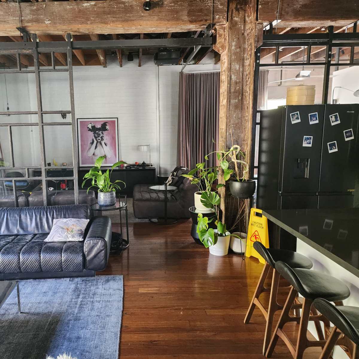 A modern living space with wooden beams, a dark leather sofa, plants, and a bar area with stools.