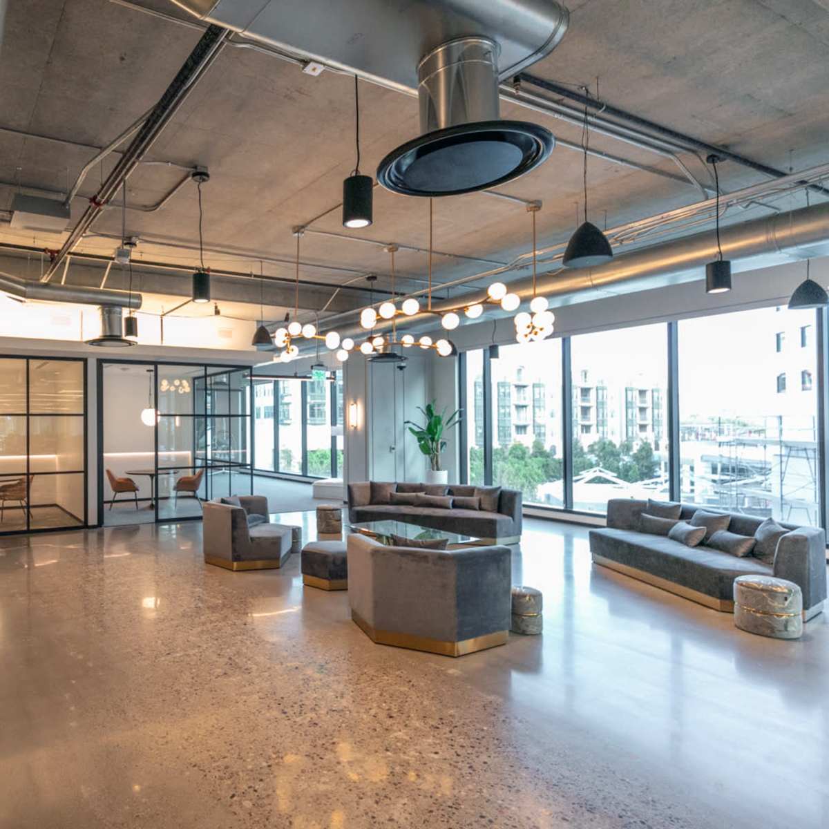 A modern office space with large windows, industrial lighting, and glass-walled meeting rooms.