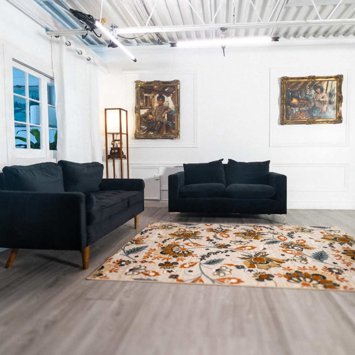 A minimalist room with two black sofas facing each other, a decorative rug on the floor, a potted plant in the corner, and framed artwork on the walls.