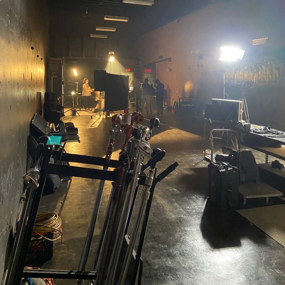 A dimly lit studio space with several lighting setups and equipment positioned along the left wall.