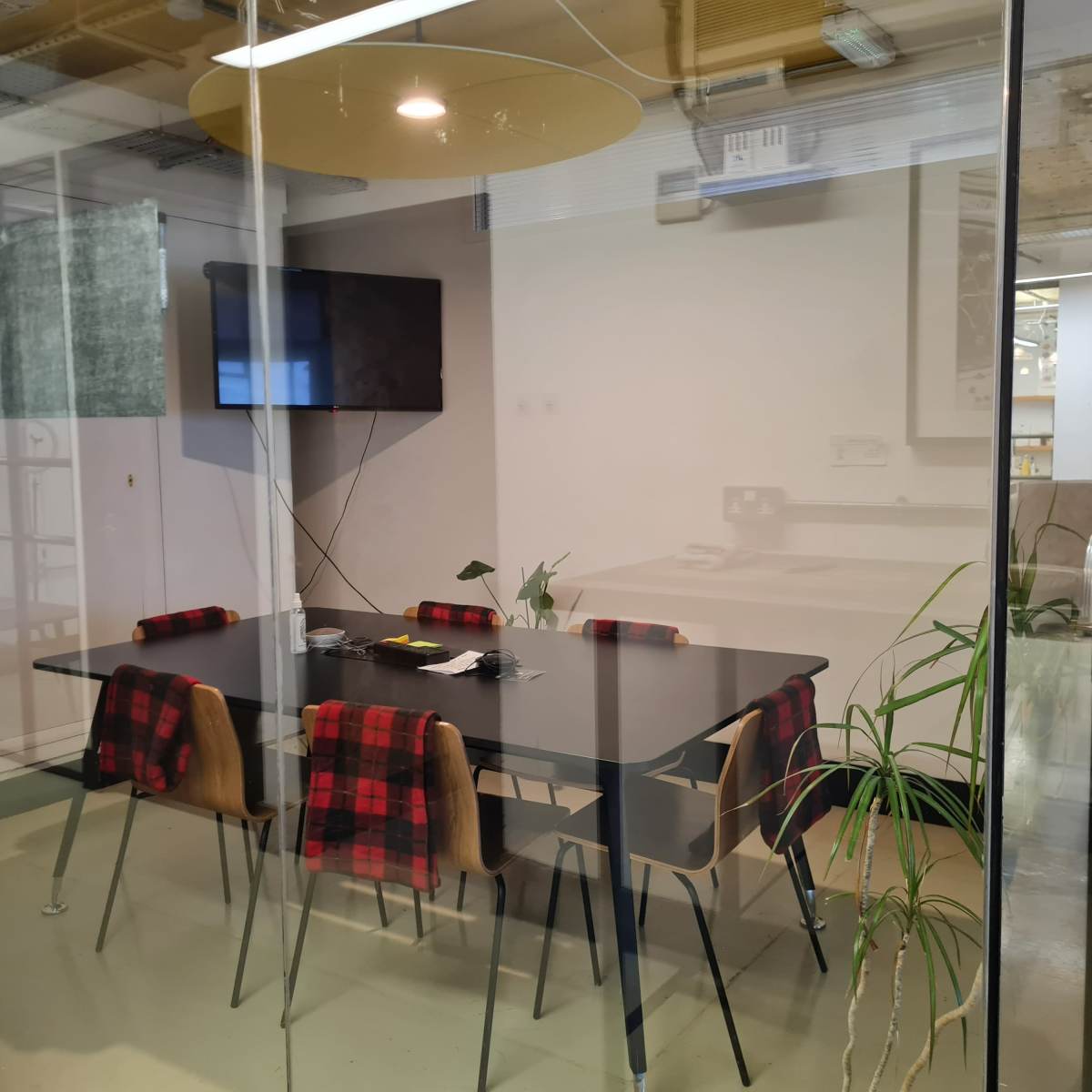 A conference room features a glass wall, a black table surrounded by chairs, and a wall-mounted television.