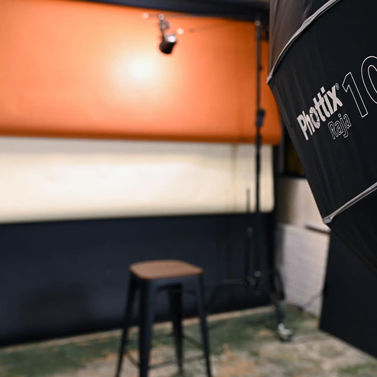 A photography studio setup with a black backdrop, a stool, and lighting equipment.