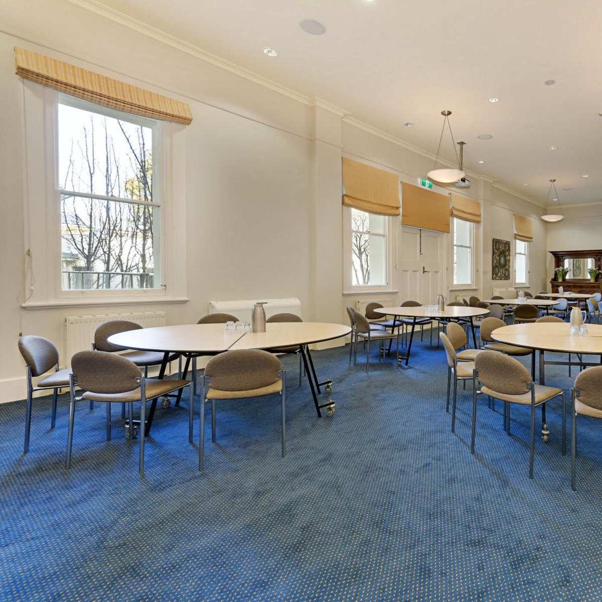 A spacious meeting room furnished with round tables and chairs, featuring large windows and a projector screen.