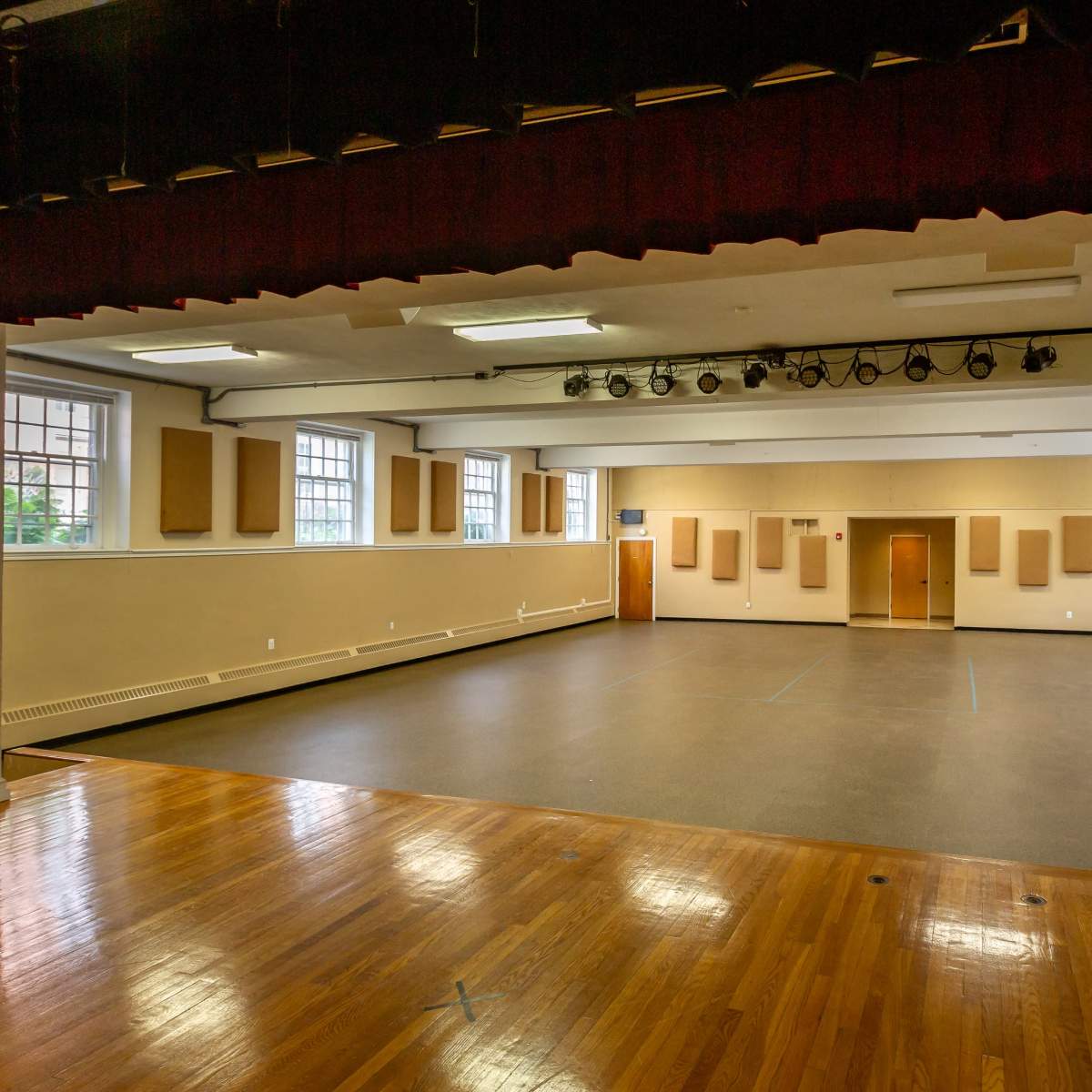 A spacious empty auditorium with a polished wooden floor, large windows, and soundproof wall panels.