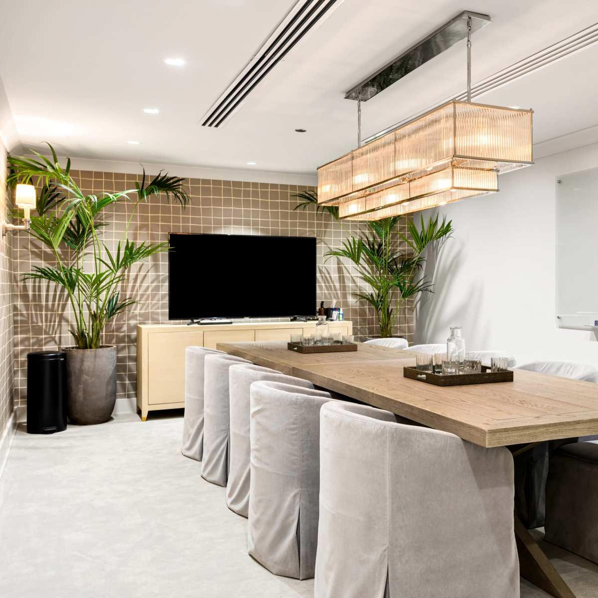 A spacious conference room features a long wooden table surrounded by upholstered chairs, a large TV on the wall, and a whiteboard.