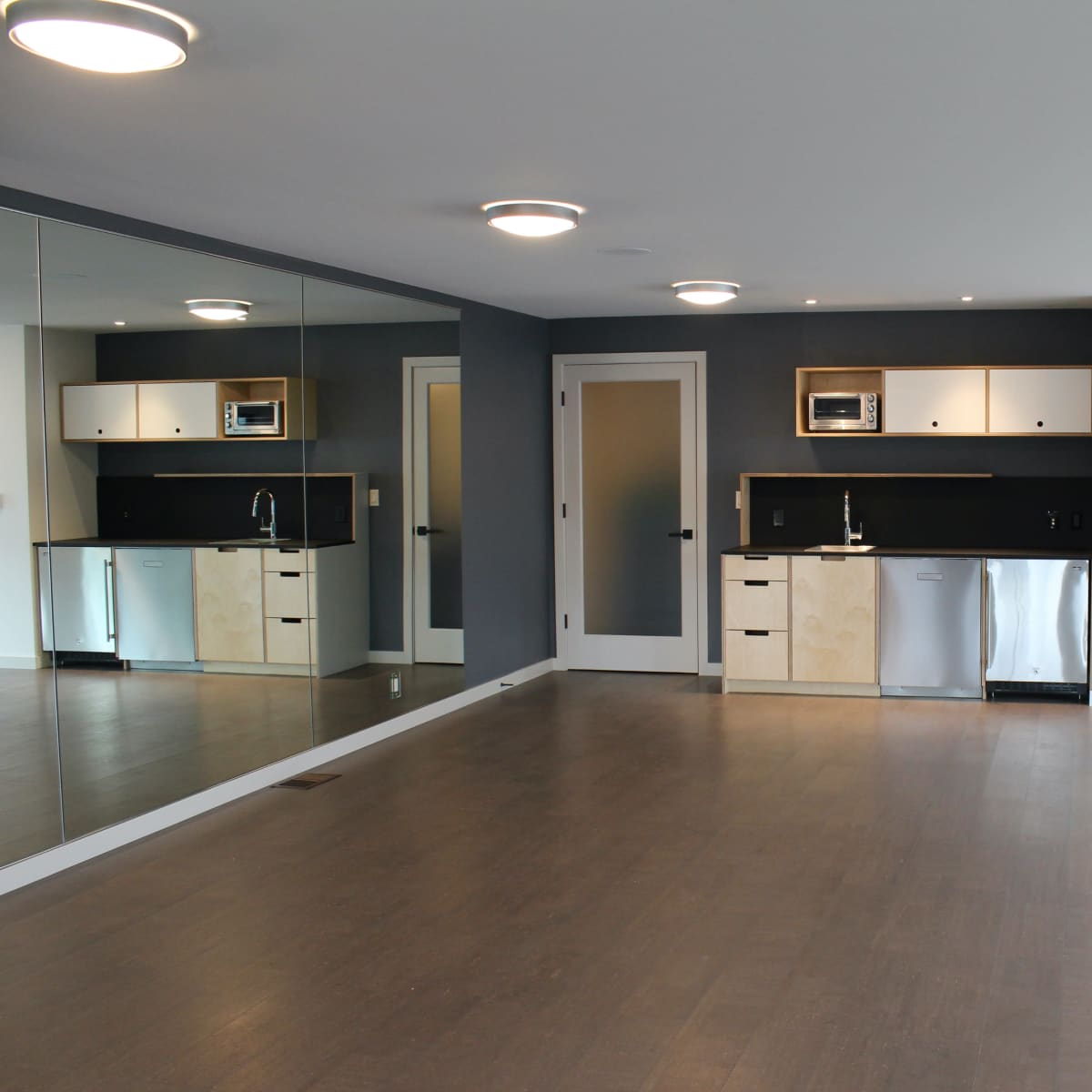 A modern, open living space with a kitchenette, large mirror on one wall, and minimalist design elements.