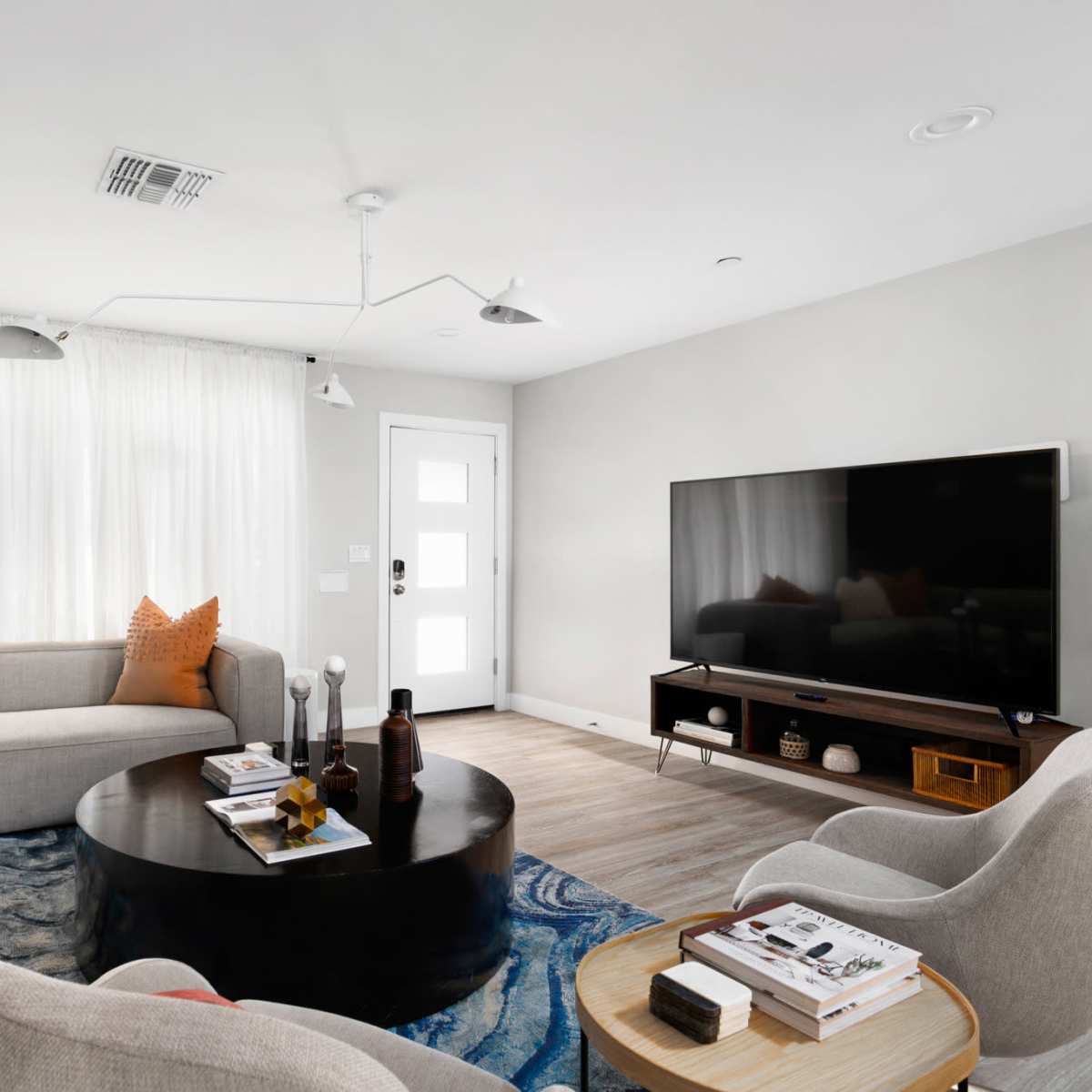 A modern living room featuring a gray sectional sofa, a round black coffee table, a large television, and a combination of light and dark decor elements.