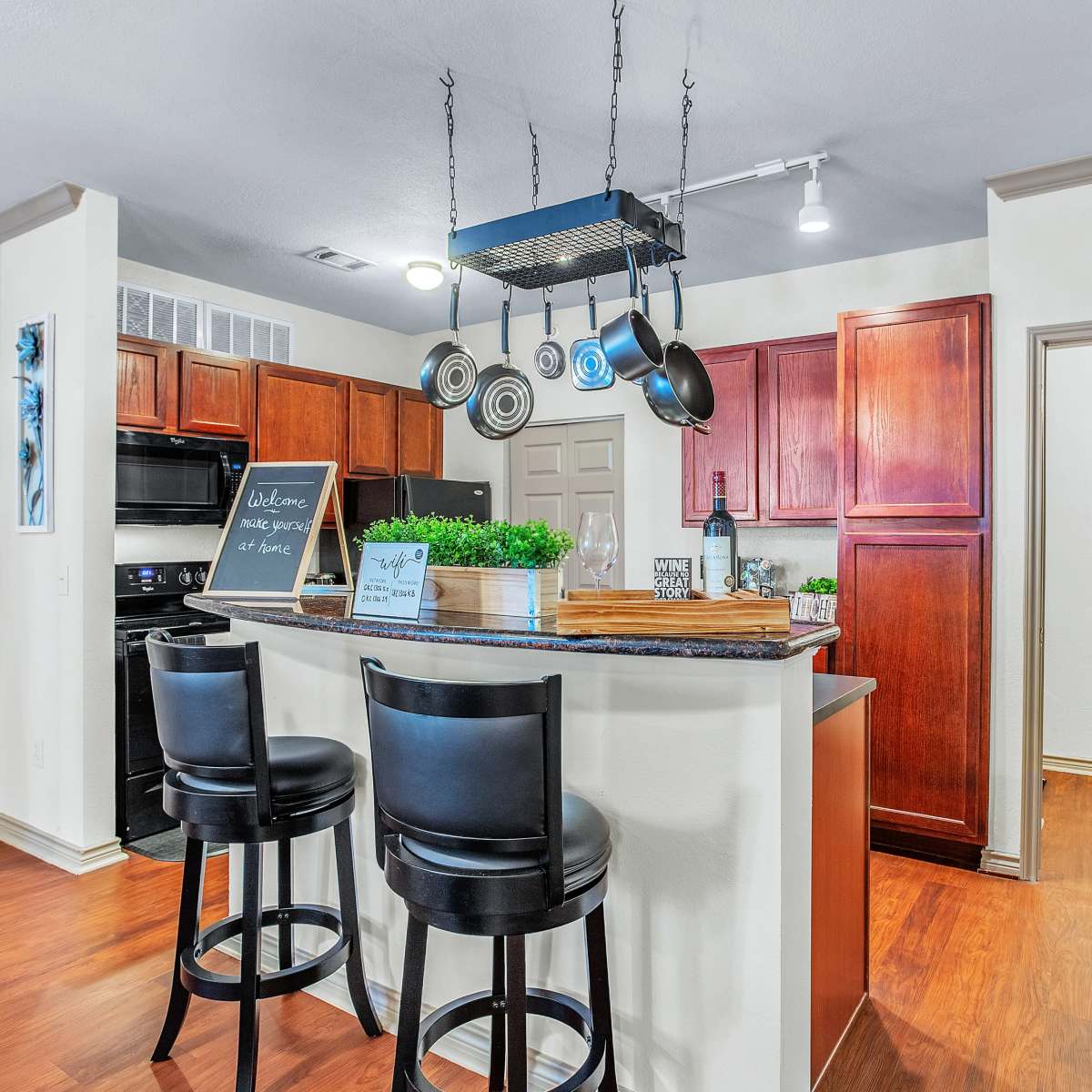 The kitchen features dark wood cabinets, a central island with bar stools, and hanging cookware above the counter.
