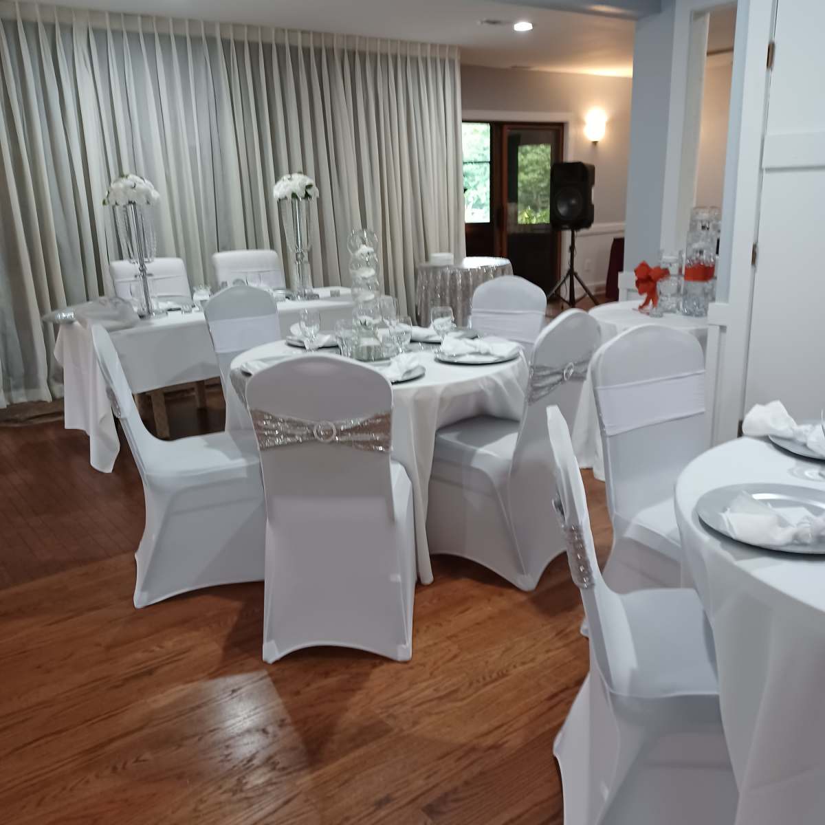 A banquet room arranged with white tablecloths and chairs adorned with decorative sashes, set for an event.