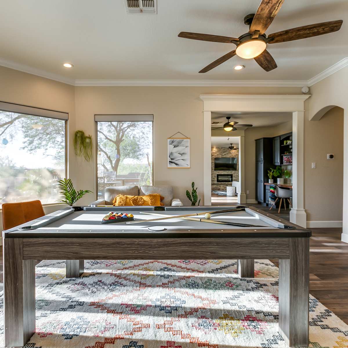 A well-lit room featuring a pool table in the center, surrounded by large windows and a seating area.