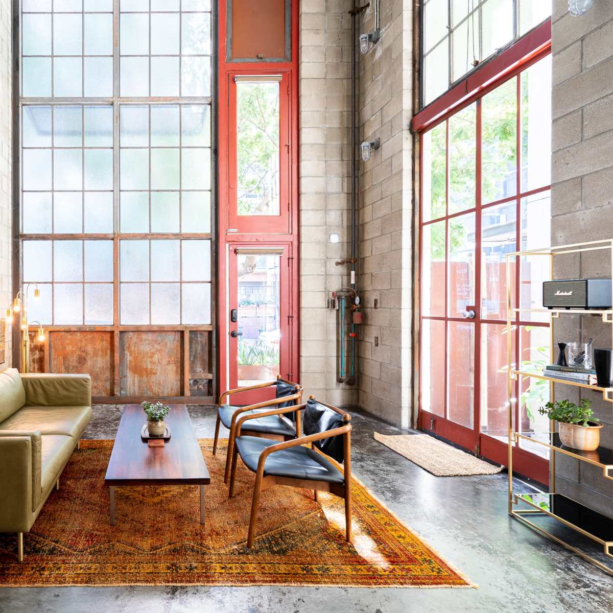 A modern living room with a green leather sofa, two black chairs, a wooden coffee table, and large windows allowing natural light to enter.