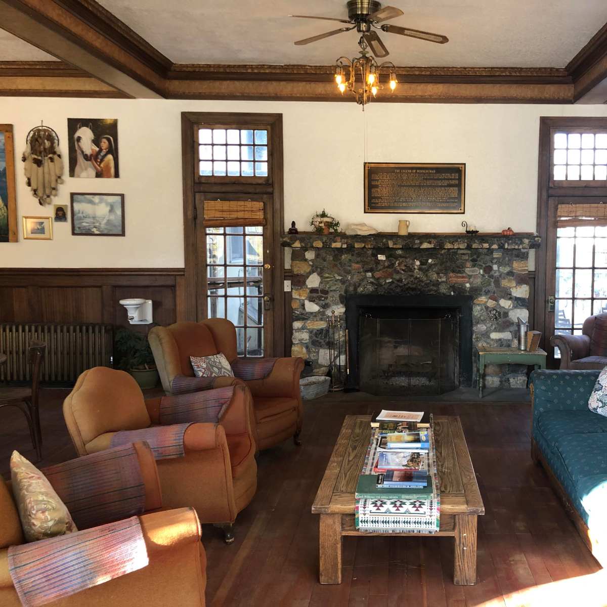 The living room features a stone fireplace surrounded by wooden walls, with various seating options, including two armchairs and a couch, arranged around a central coffee table.