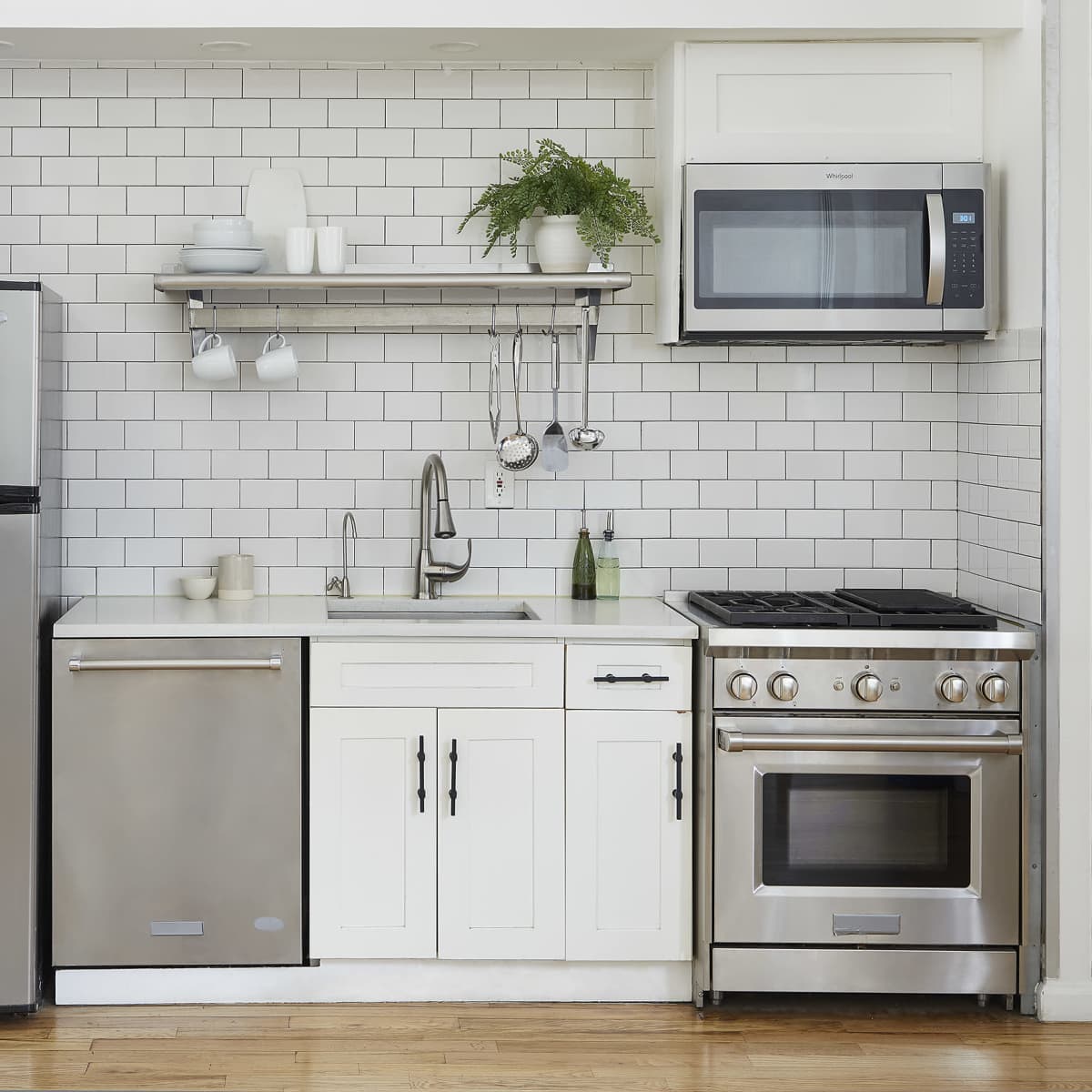 A modern kitchen with stainless steel appliances, including a refrigerator, dishwasher, and range, set against a white tiled backsplash.